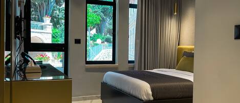 Un dormitorio moderno con una cama grande, un escritorio y dos ventanas arqueadas que dan a zonas verdes.