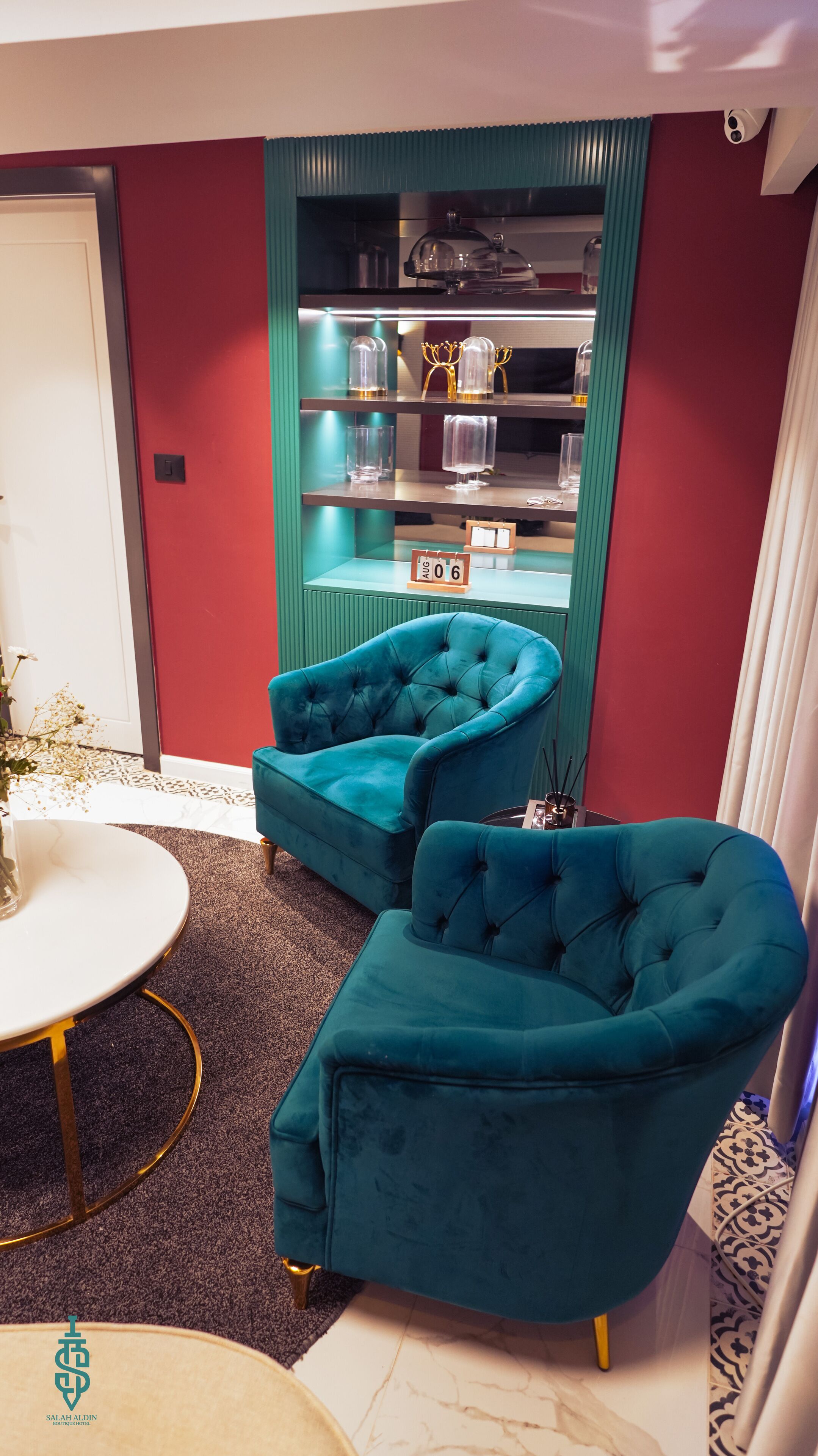 Una habitación con sillones tapizados en color turquesa, una mesa redonda blanca y un estante con objetos decorativos.