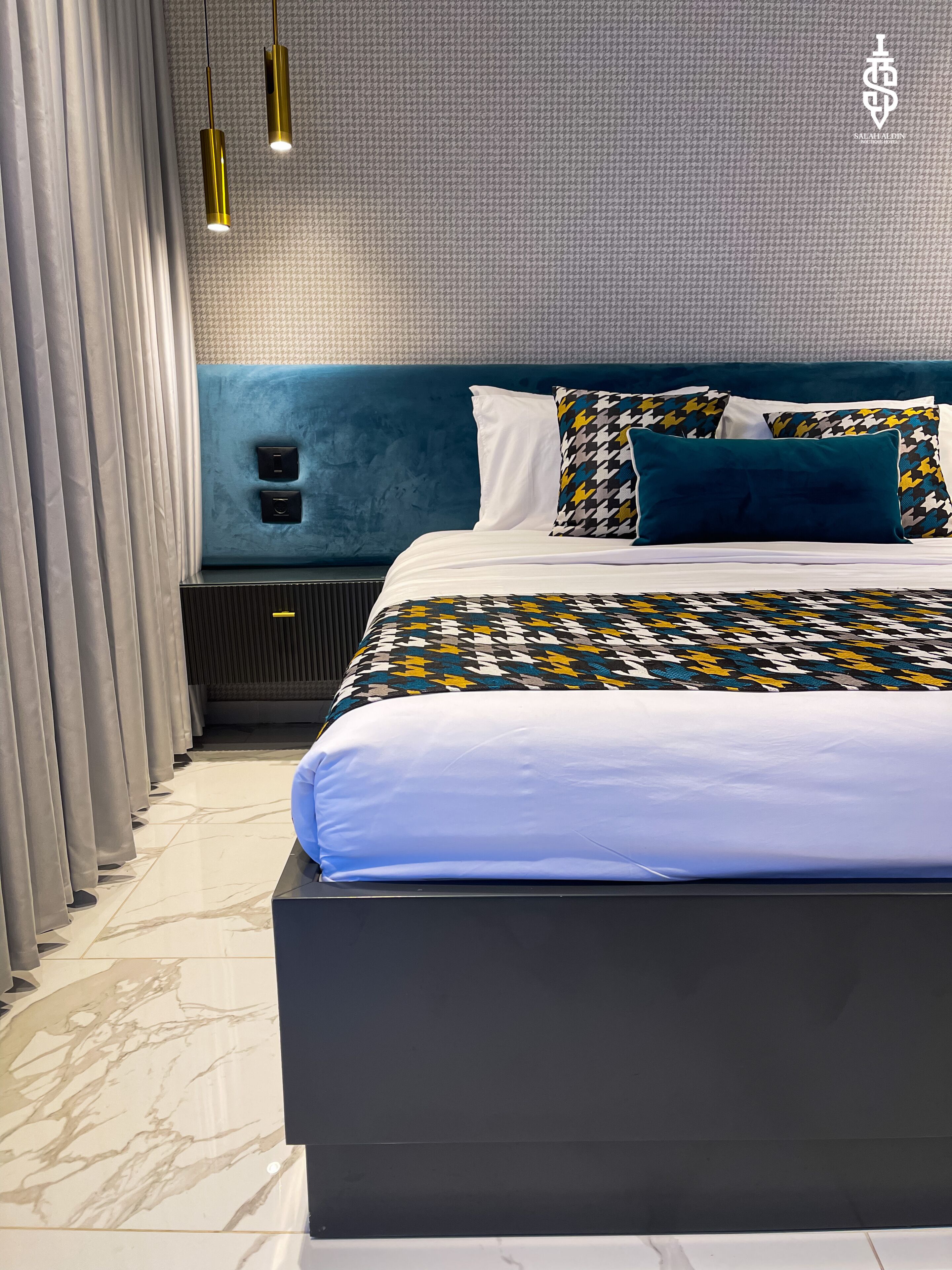 A modern bedroom with a large bed, a blue headboard, and patterned bedding.