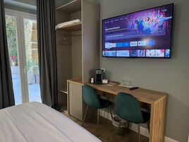 Una habitación de hotel con cama, un escritorio con dos sillas, un televisor mostrando una película y un armario con perchero.