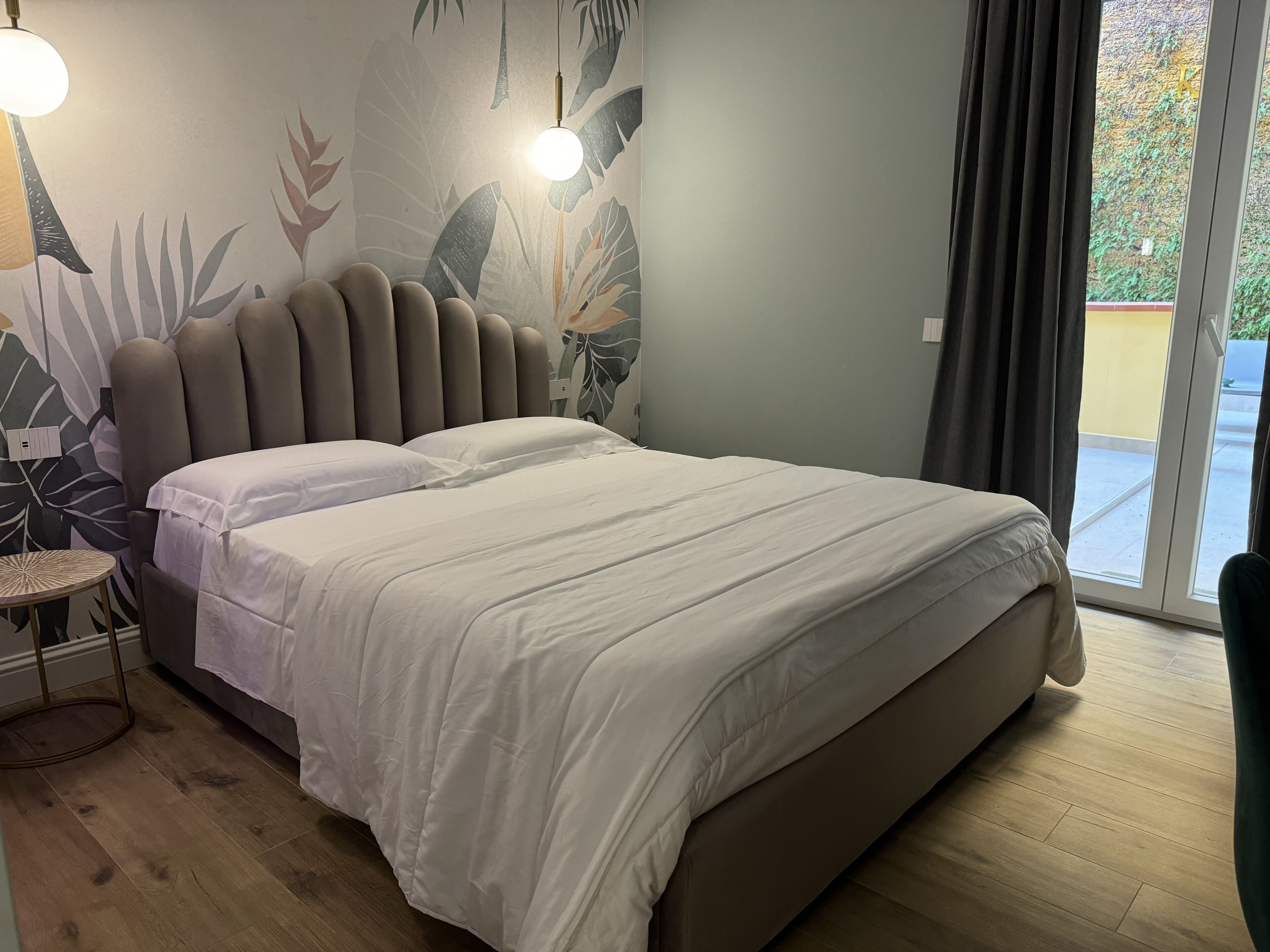 Una camera da letto con un letto, un tavolino rotondo e una parete decorata con un motivo a foglia tropicale.
