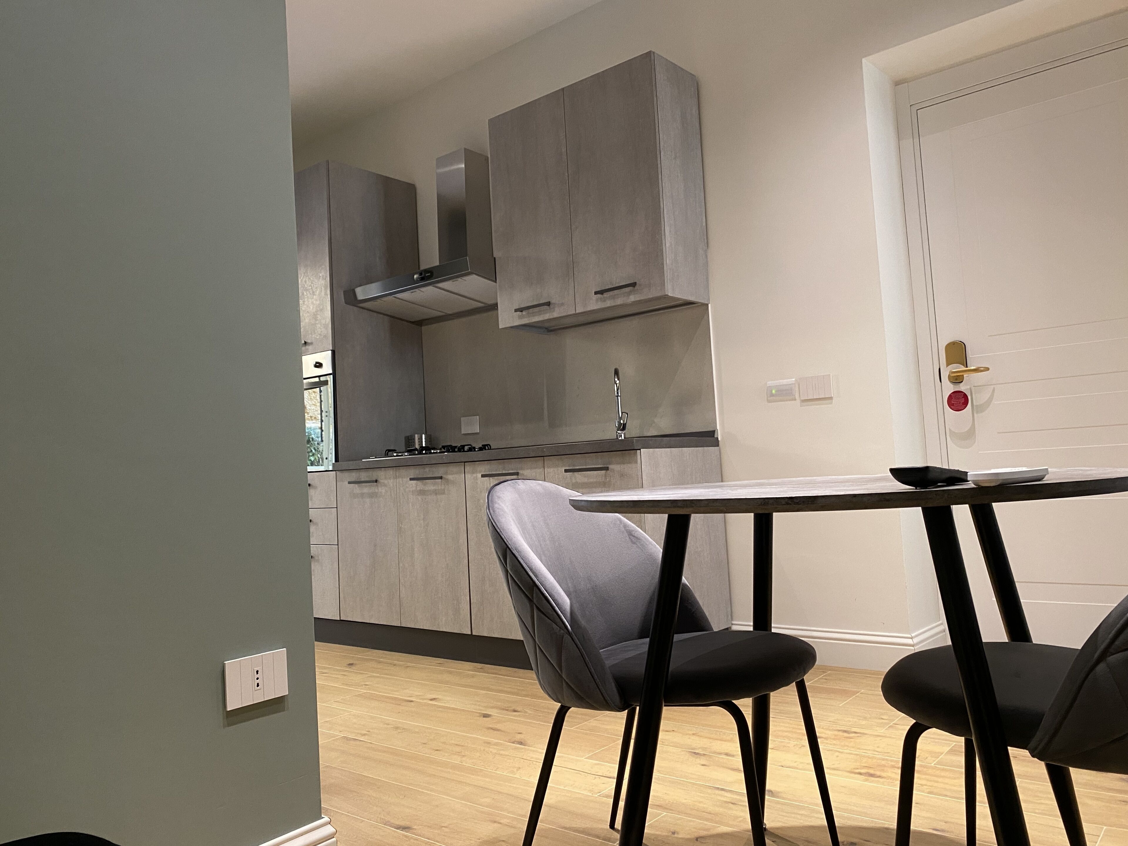 A modern kitchen with grey cabinets, a stainless steel range hood, and a wooden floor.