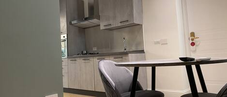 A modern kitchen with grey cabinets, a stainless steel range hood, and a wooden floor.
