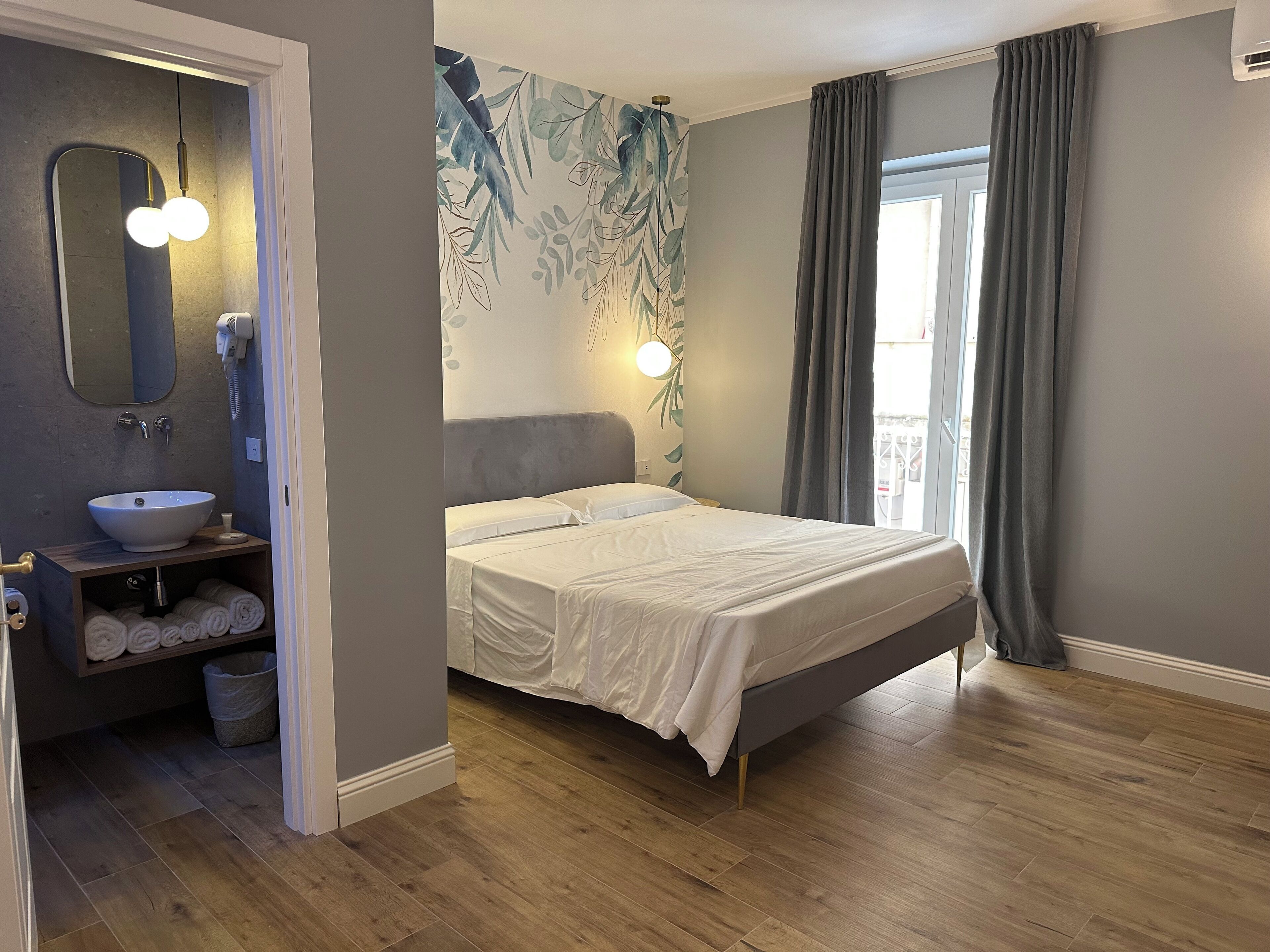 A modern bedroom with a large bed, a bathroom with a sink and mirror, and a view of the outdoors.