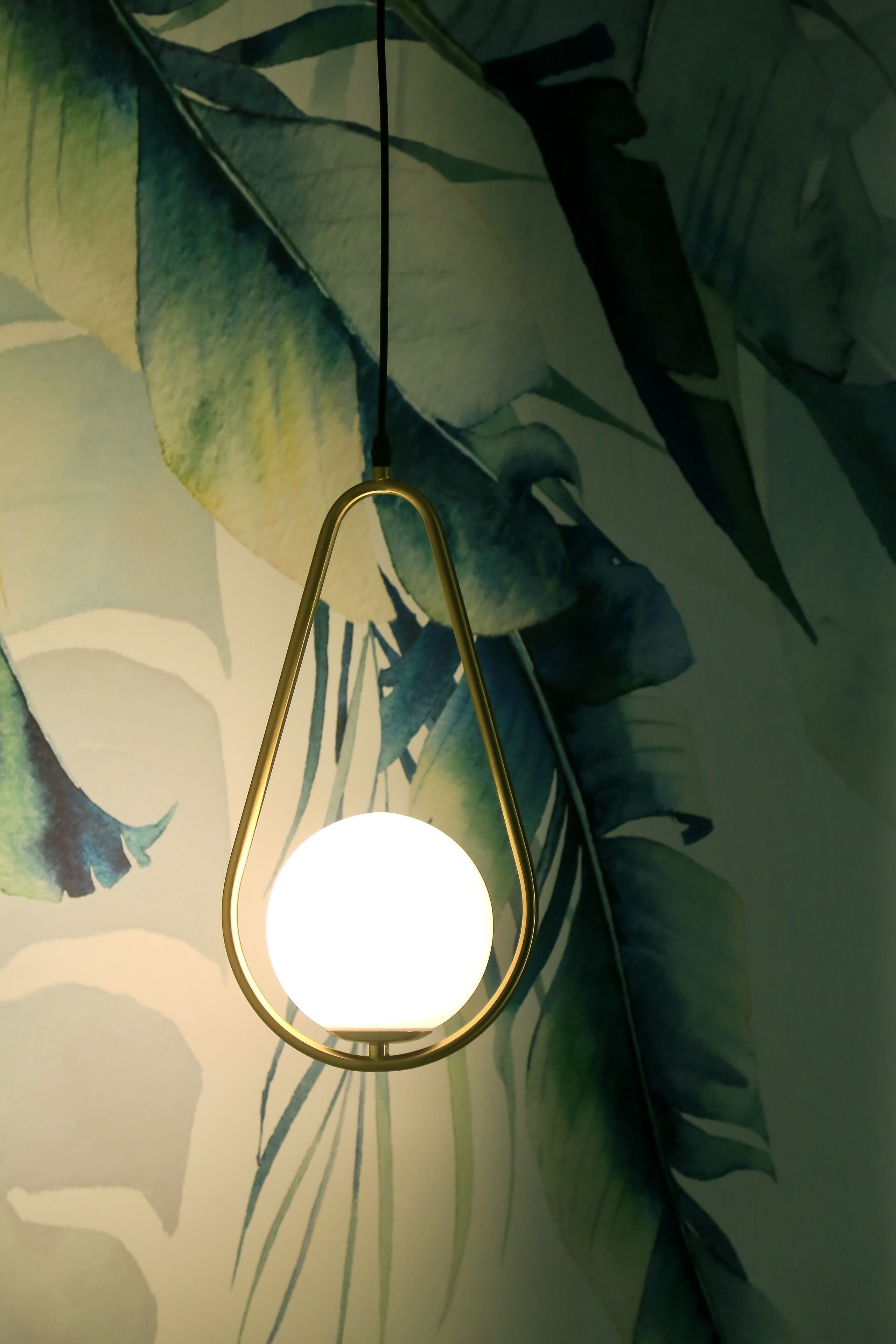 Een hanglamp met gouden frame hangt aan een plafond met bladmotief.