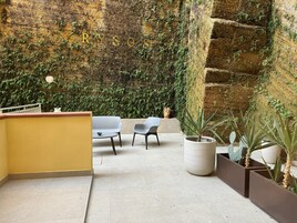 A modern indoor space with a yellow wall, a reception desk, two chairs, and a large potted plant.