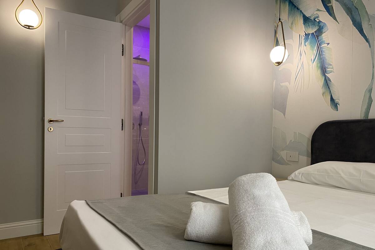 A hotel room with a bed, a shower, and a wall with a feather painting.