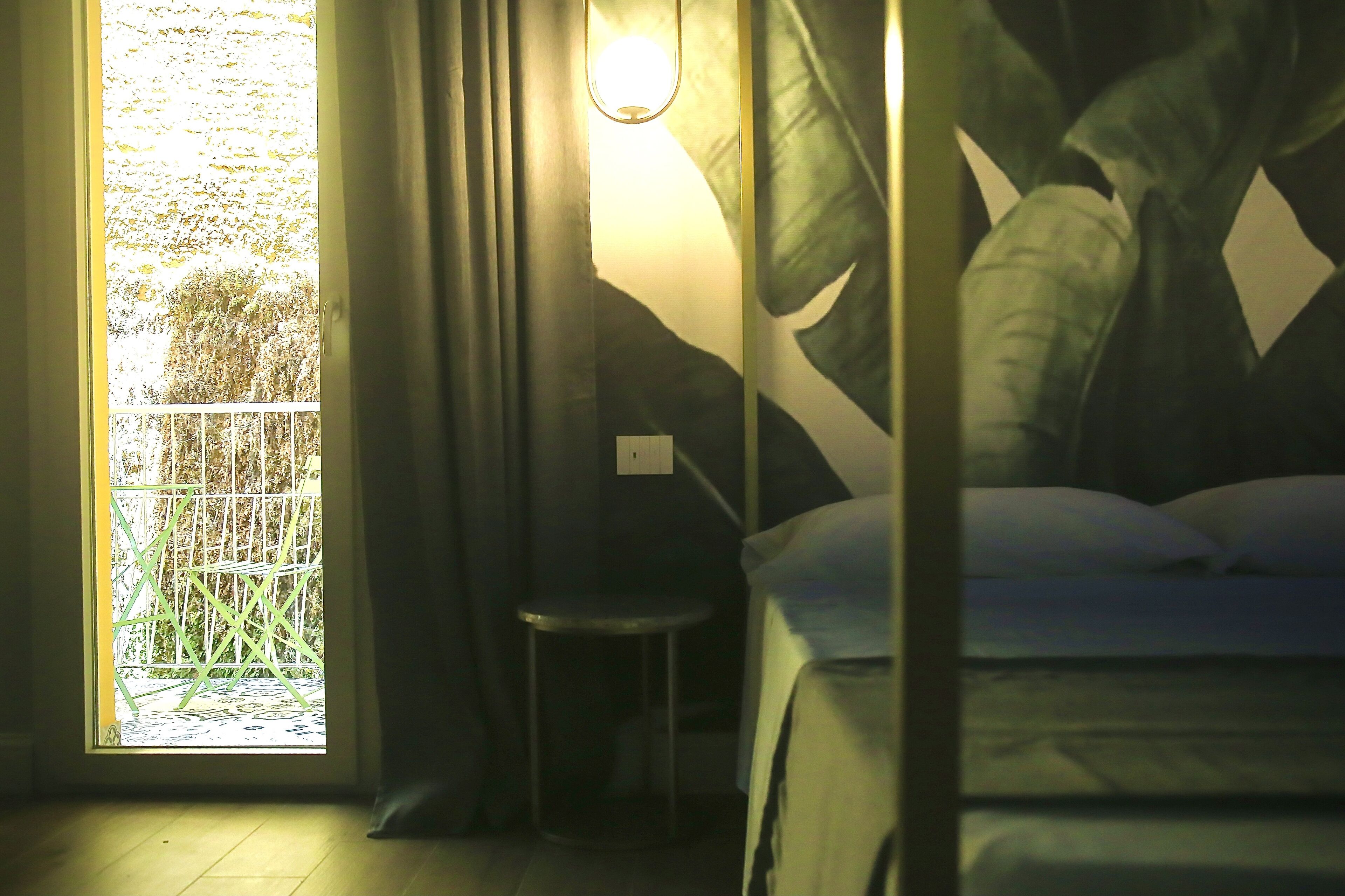 Quarto com cama, uma cadeira e janela com vista para vegetação.