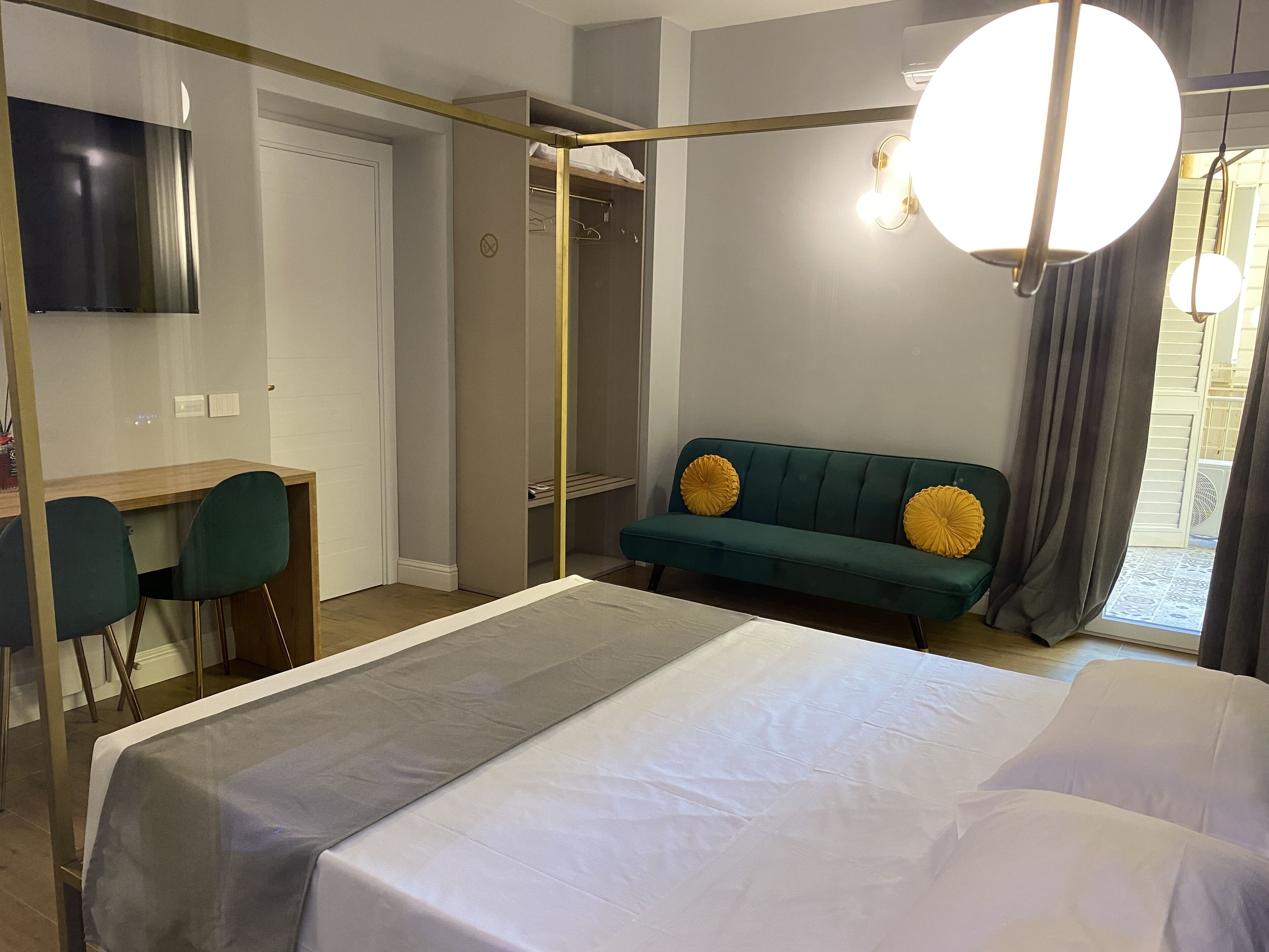 Une chambre moderne avec un lit, un bureau, un canapé vert agrémenté de coussins jaunes et un grand luminaire rond.