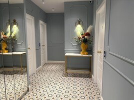 A hallway with patterned flooring, a mirror, and two vases with flowers on a console table.