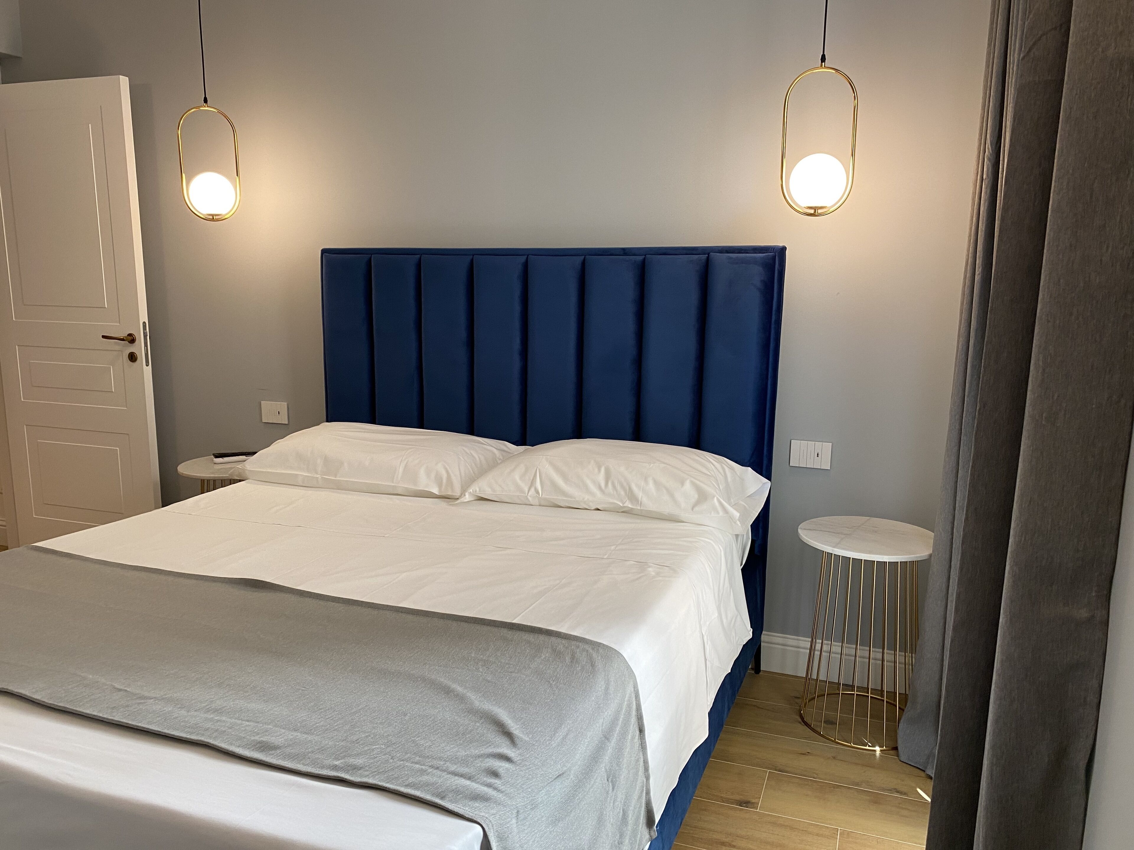 A neatly made bed with a blue headboard, two bedside tables, and a small round table.