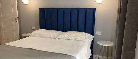 A neatly made bed with a blue headboard, two bedside tables, and a small round table.