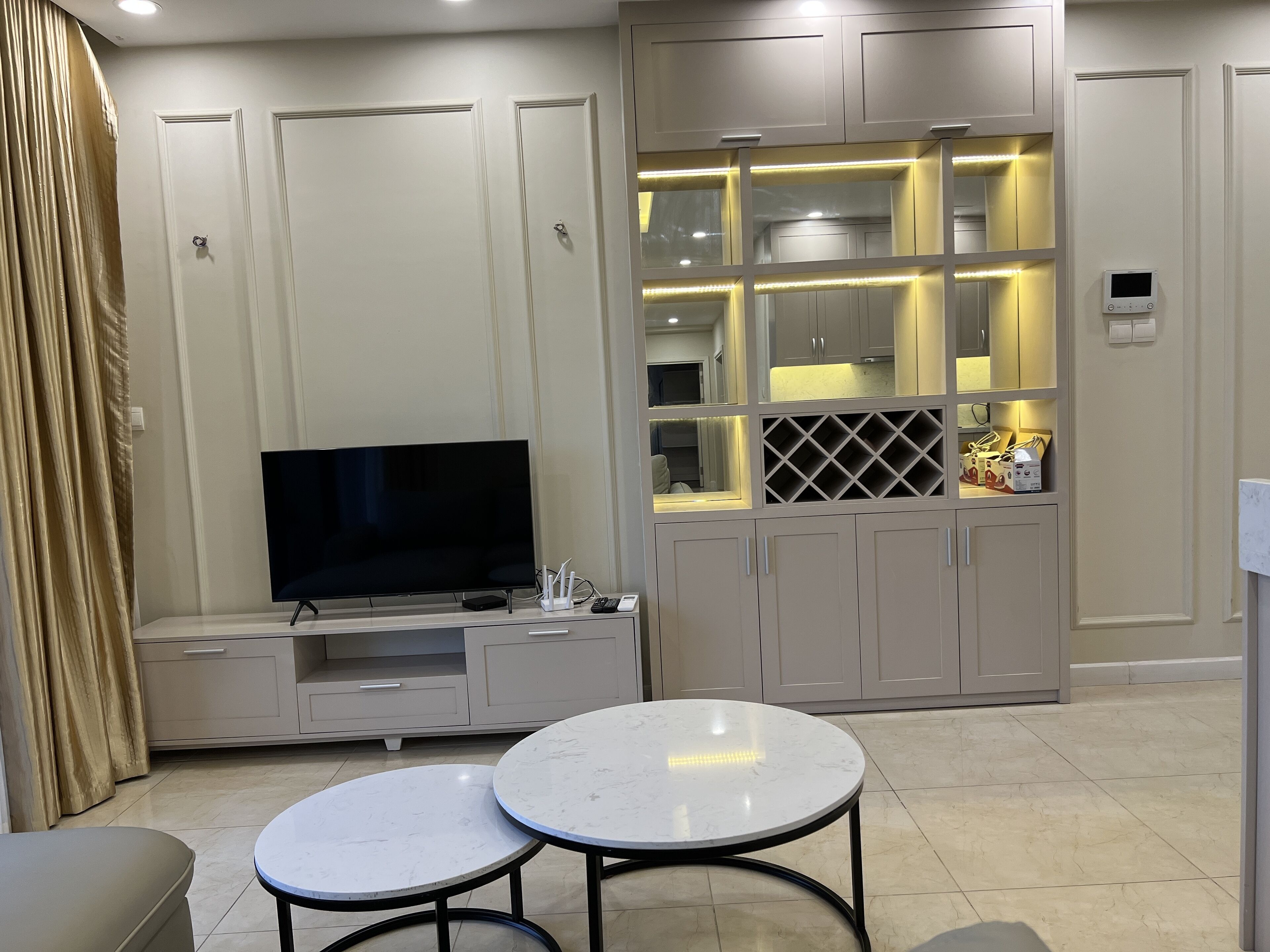 A modern living room with a flat-screen TV, two round tables, and a built-in entertainment unit.