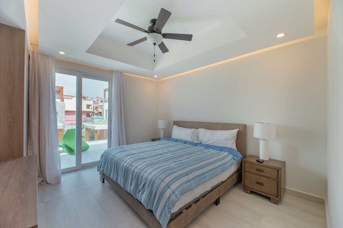 Ein Schlafzimmer mit Bett, Nachttischen, Deckenventilator und Blick ins Freie.
