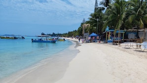 Une plage à l’eau turquoise et limpide, un rivage sablonneux et plusieurs bateaux ancrés à proximité.