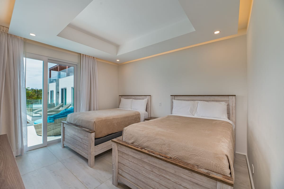 Ein Schlafzimmer mit zwei Betten, einer Glasschiebetür zu einem Balkon und einem modernen Deckenstil.