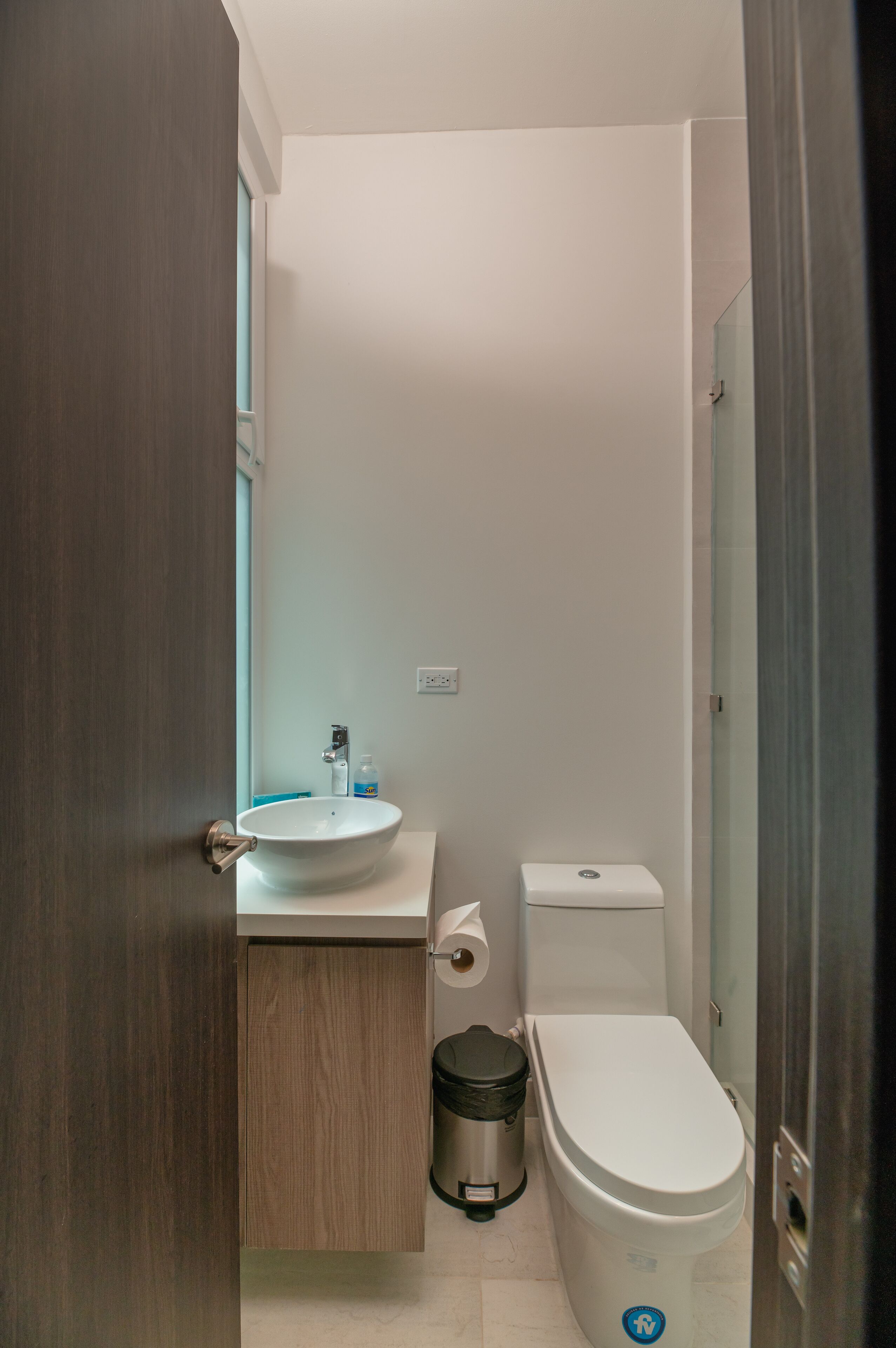 Une petite salle de bain avec un lavabo blanc, des toilettes et une poubelle.