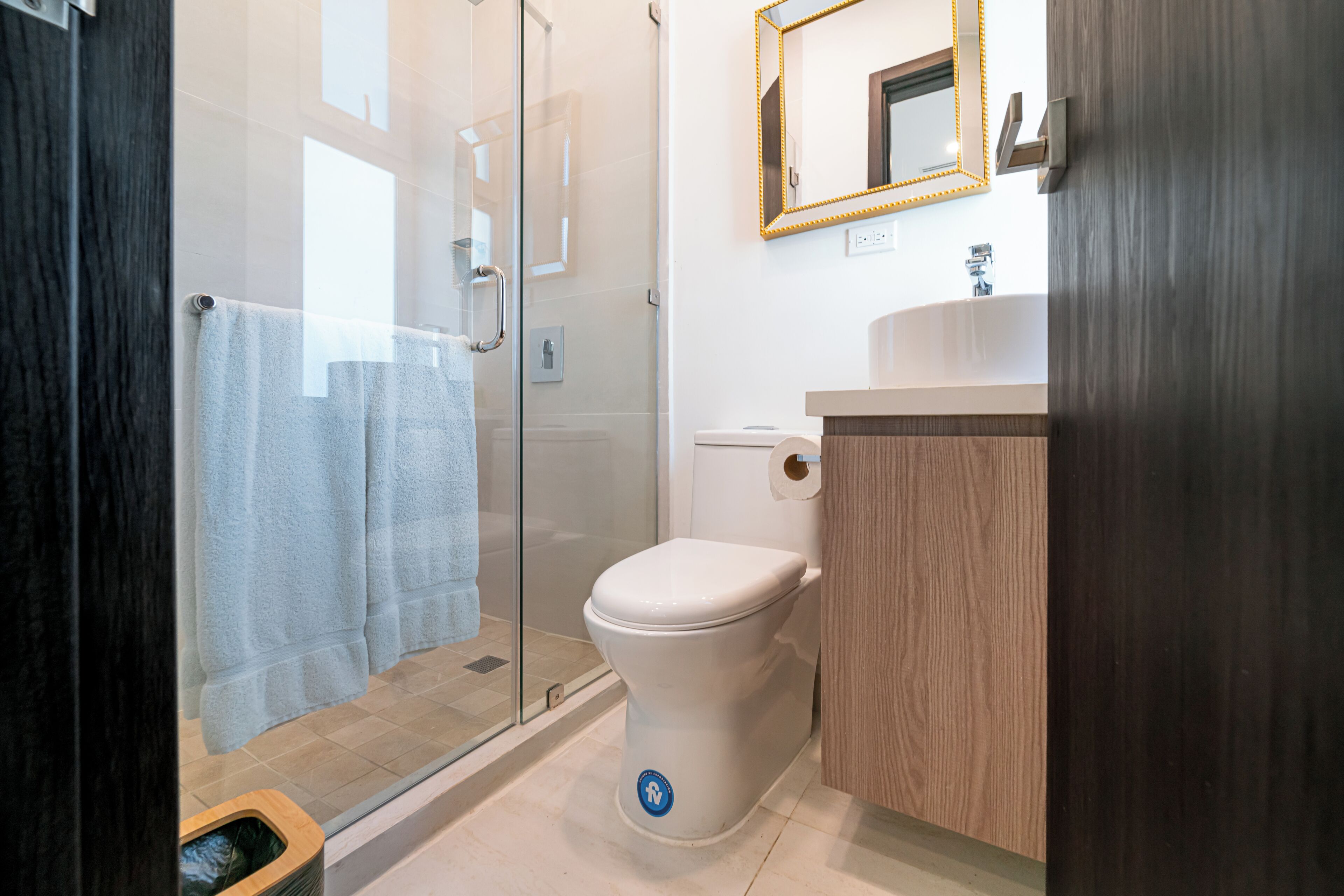 A modern bathroom with a glass shower enclosure, a toilet, and a wooden vanity.