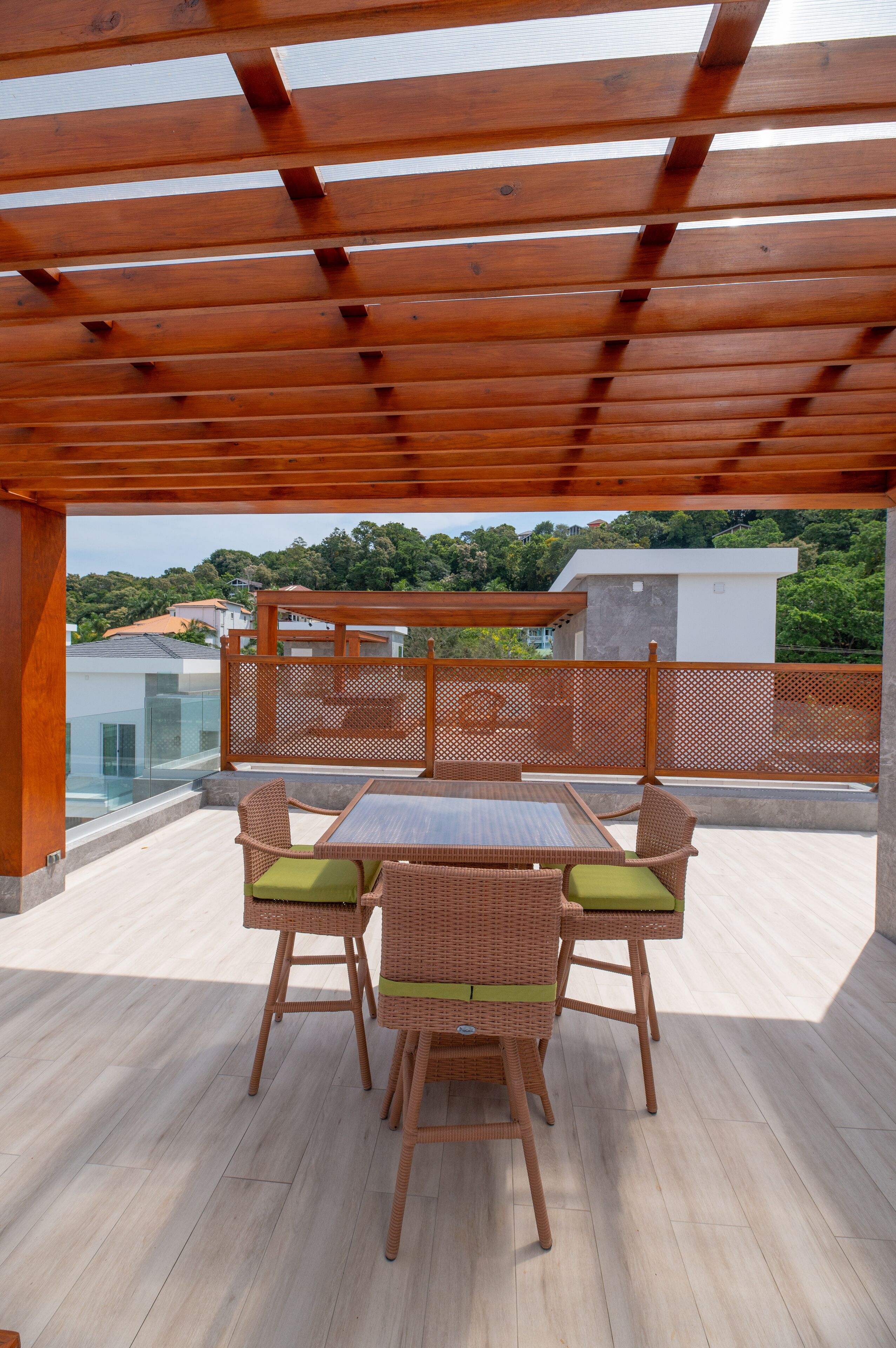 A covered outdoor patio with a wooden table and wicker chairs, overlooking a residential area.