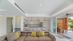 A modern living room with a beige sectional sofa, a small coffee table, and a dining area with a kitchen in the background.