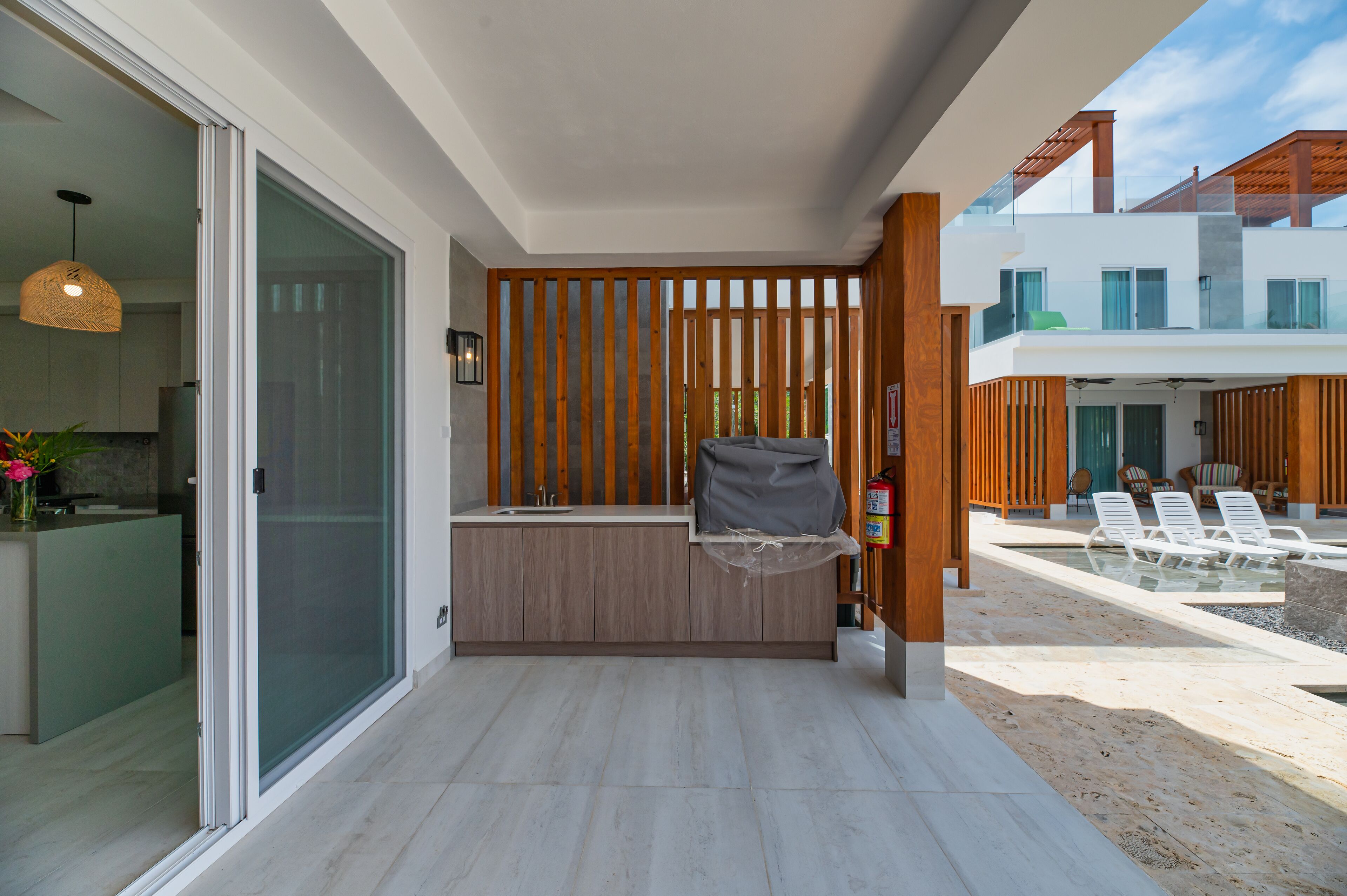 A modern kitchen with a sliding glass door leading to a balcony with a pool and lounge chairs.