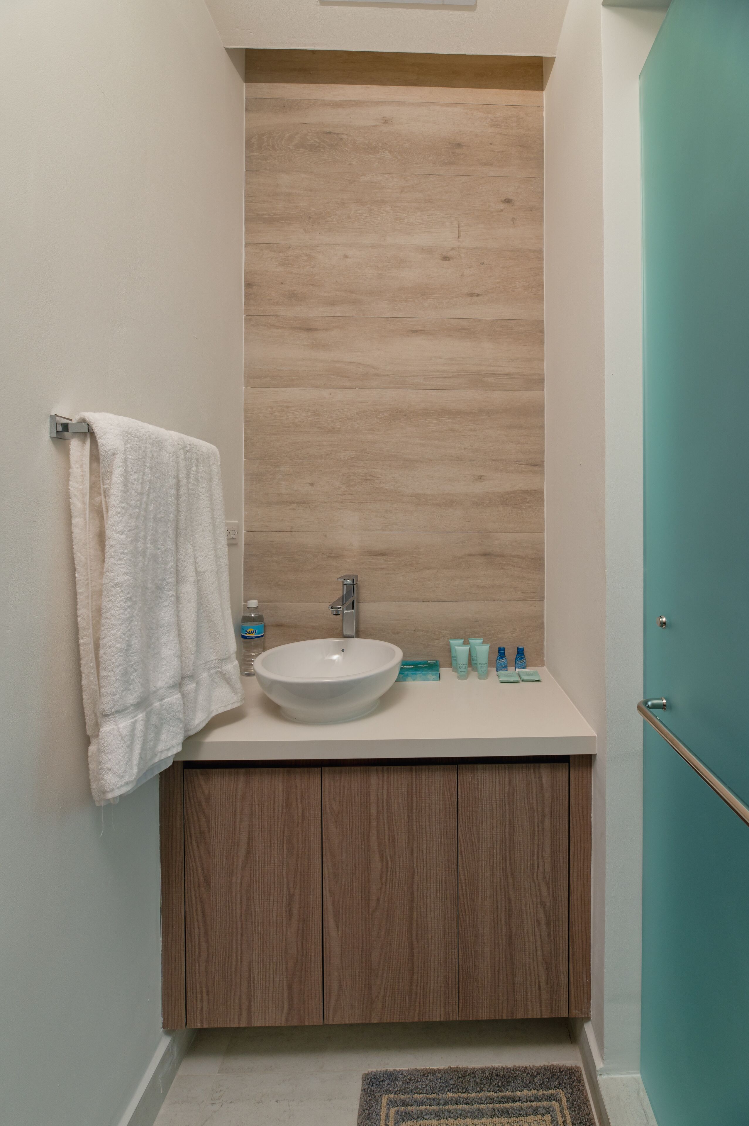 A bathroom with a white sink, wooden vanity, and a teal door.