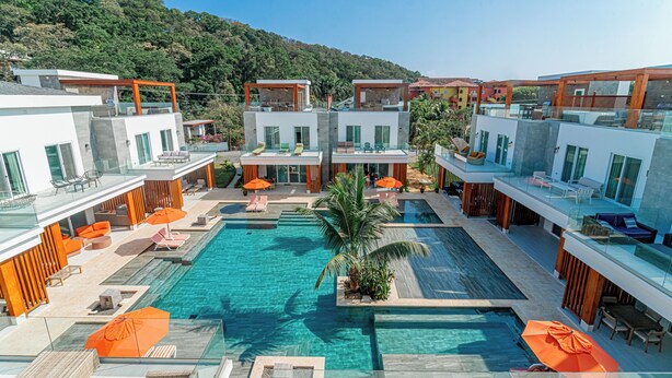 Un hôtel moderne doté d’une piscine centrale, d’un espace extérieur aménagé et offrant une vue sur une colline boisée.