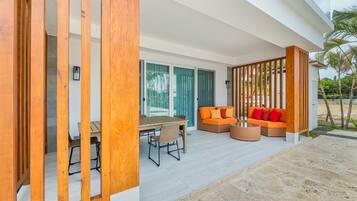 A modern outdoor seating area with a wooden table and chairs, a sofa with orange cushions, and a wicker coffee table.