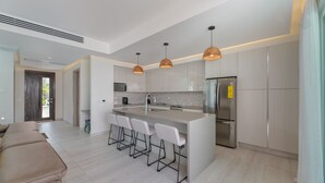 Une cuisine moderne dotée d’un îlot central, de tabourets de bar, d’appareils électroménagers en acier inoxydable et de luminaires suspendus.