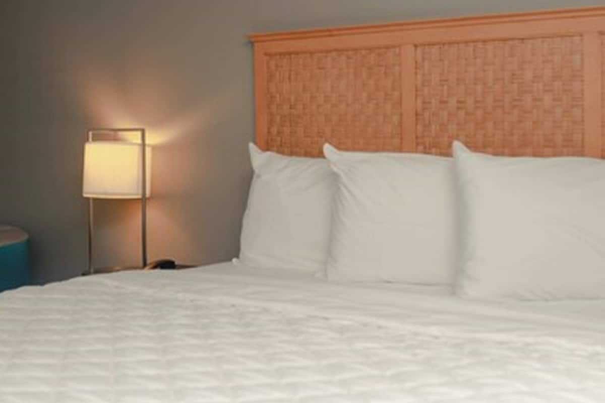 A neatly made bed with white linens, a wooden headboard, and a bedside lamp on a nightstand.
