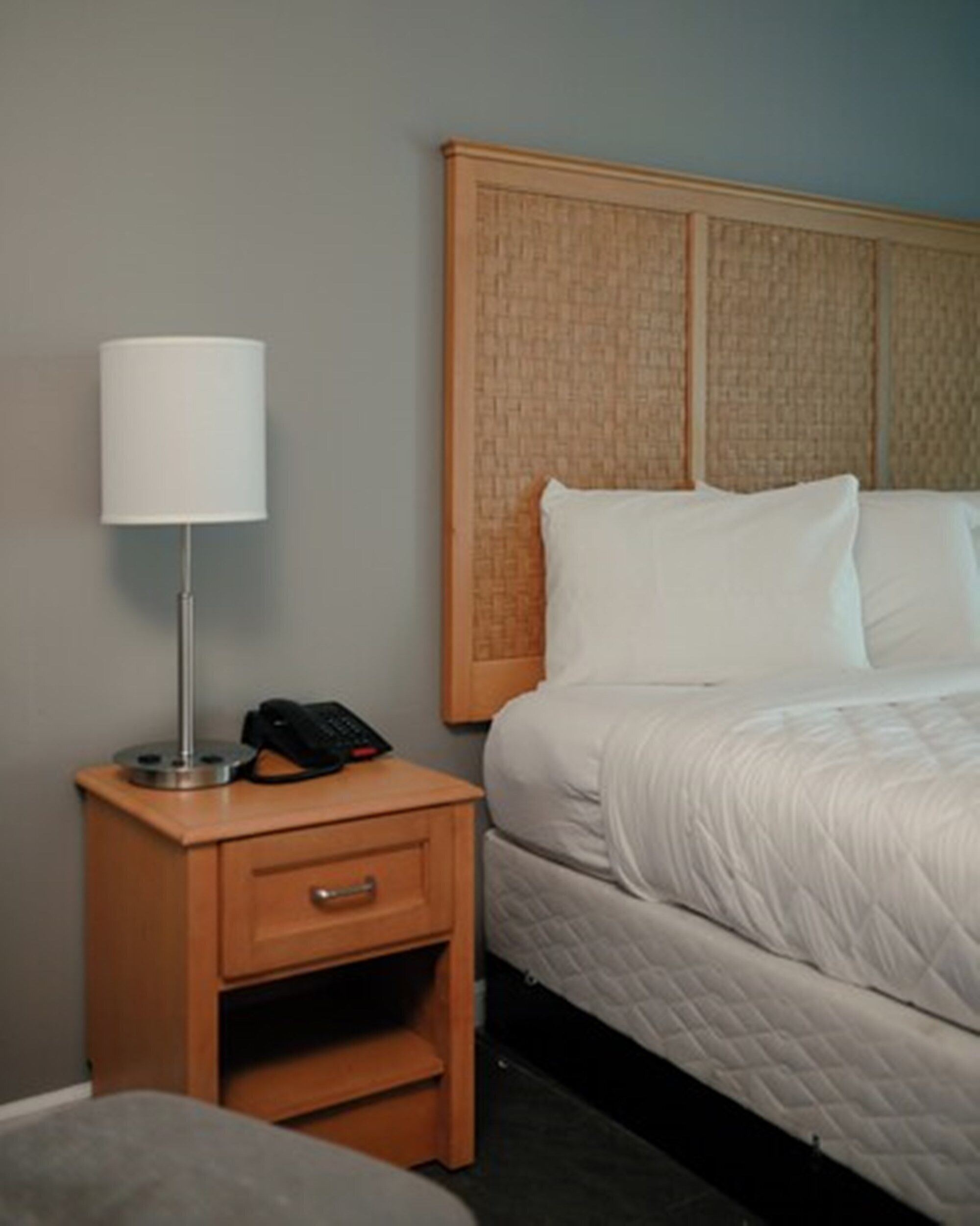 A hotel room with a bed, a nightstand with a lamp, and a drawer.