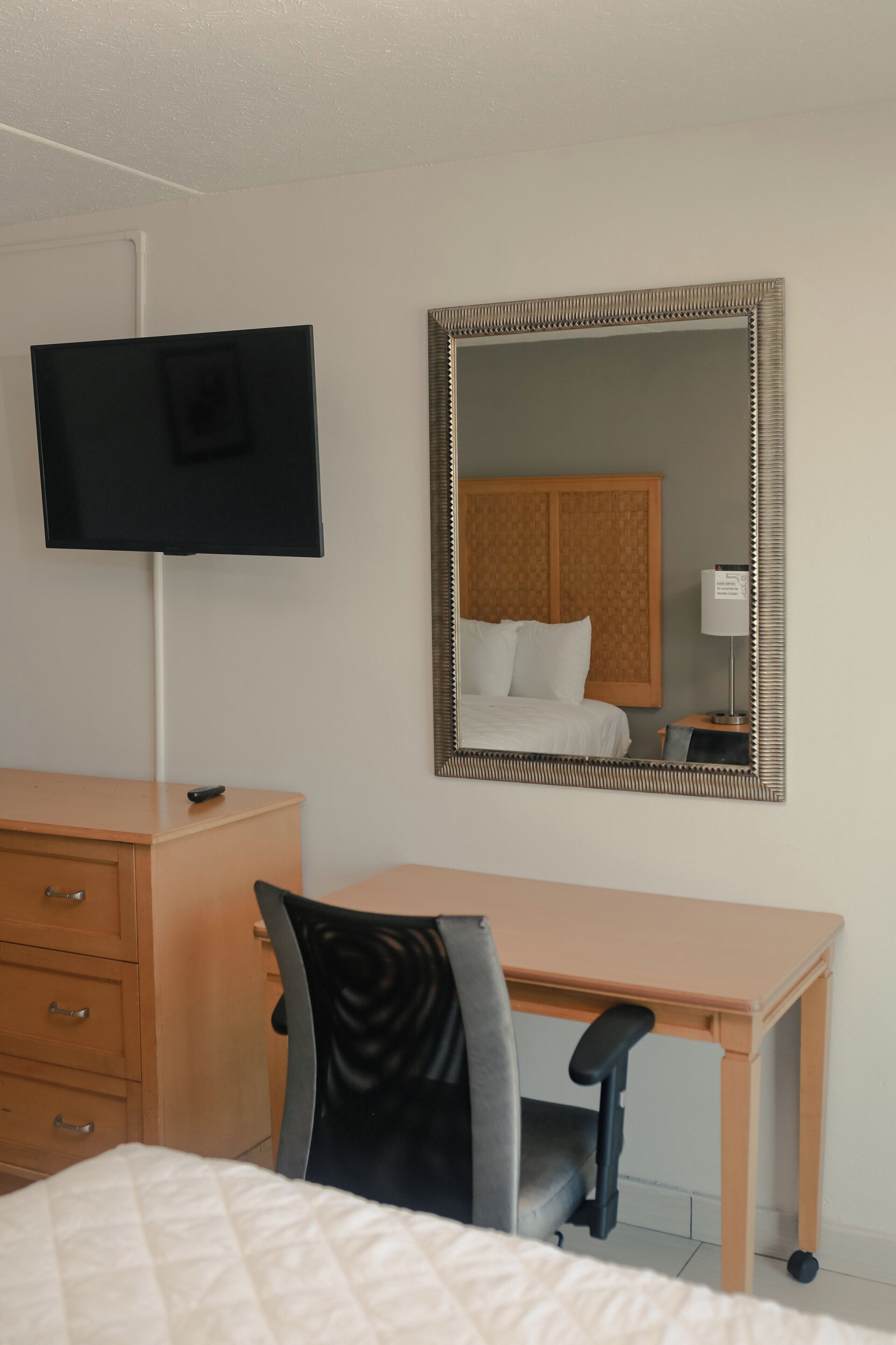 Une chambre d’hôtel équipée d’un lit, d’un bureau, d’une chaise, d’une télévision et d’un grand miroir.