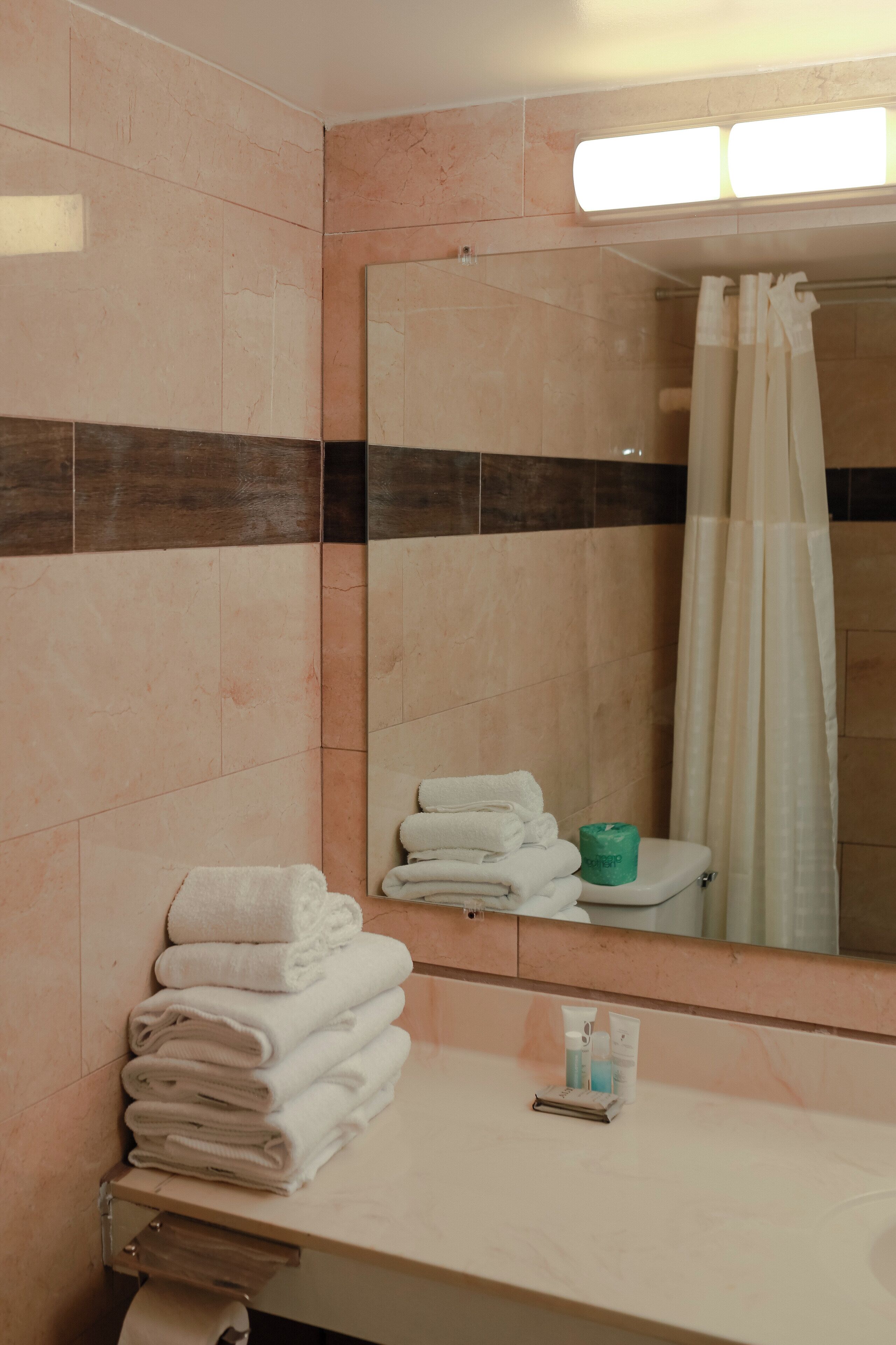 Un baño con una pila de toallas dobladas, un inodoro, un espejo y una cortina de ducha.