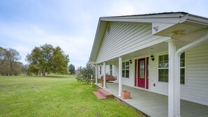 Uma casa branca com porta vermelha, varanda e um gramado.