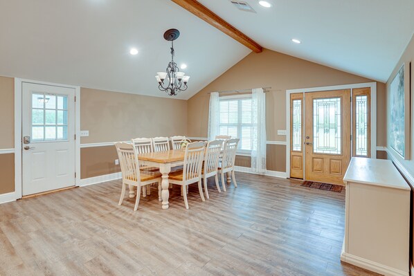 A spacious dining area with a wooden table and chairs, a chandelier, and large windows with curtains.