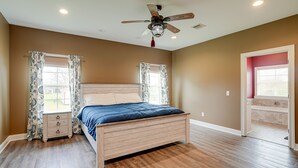 Quarto com cama de madeira, ventoinha no teto e janela com cortinas estampadas.