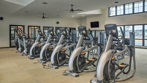 A gym with multiple stationary bikes, large windows, and ceiling fans.