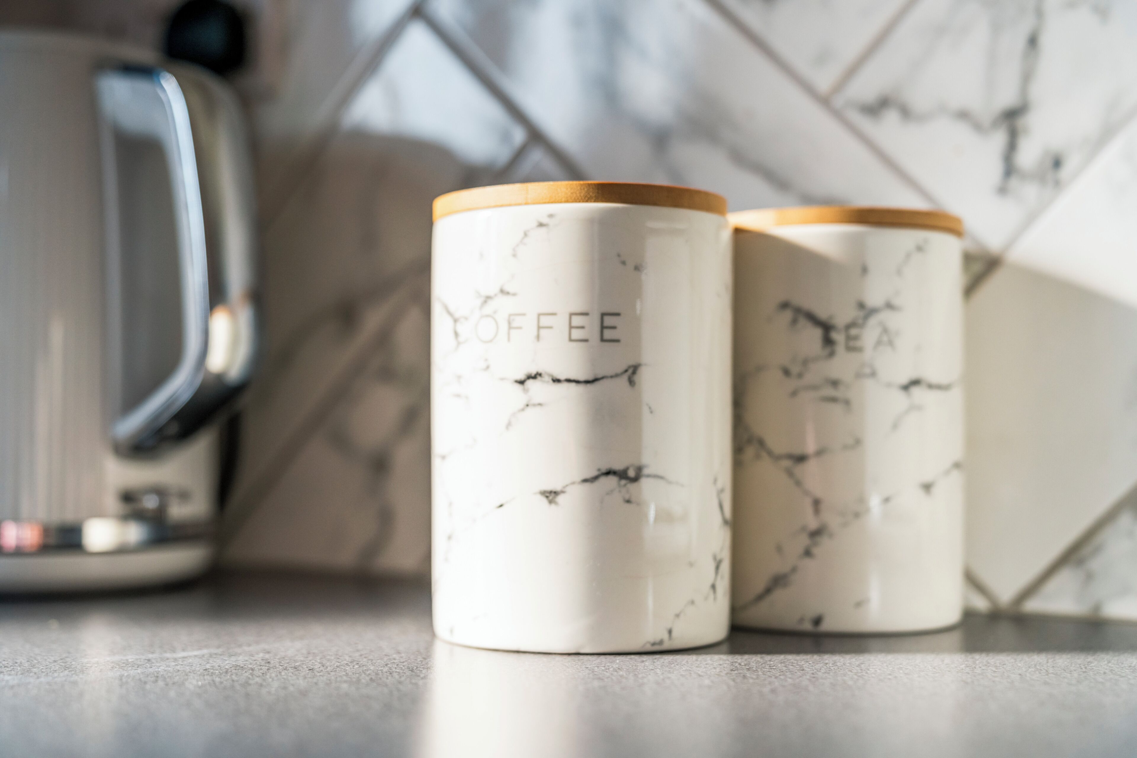 Two white coffee mugs with marble patterns and wooden lids on a countertop.