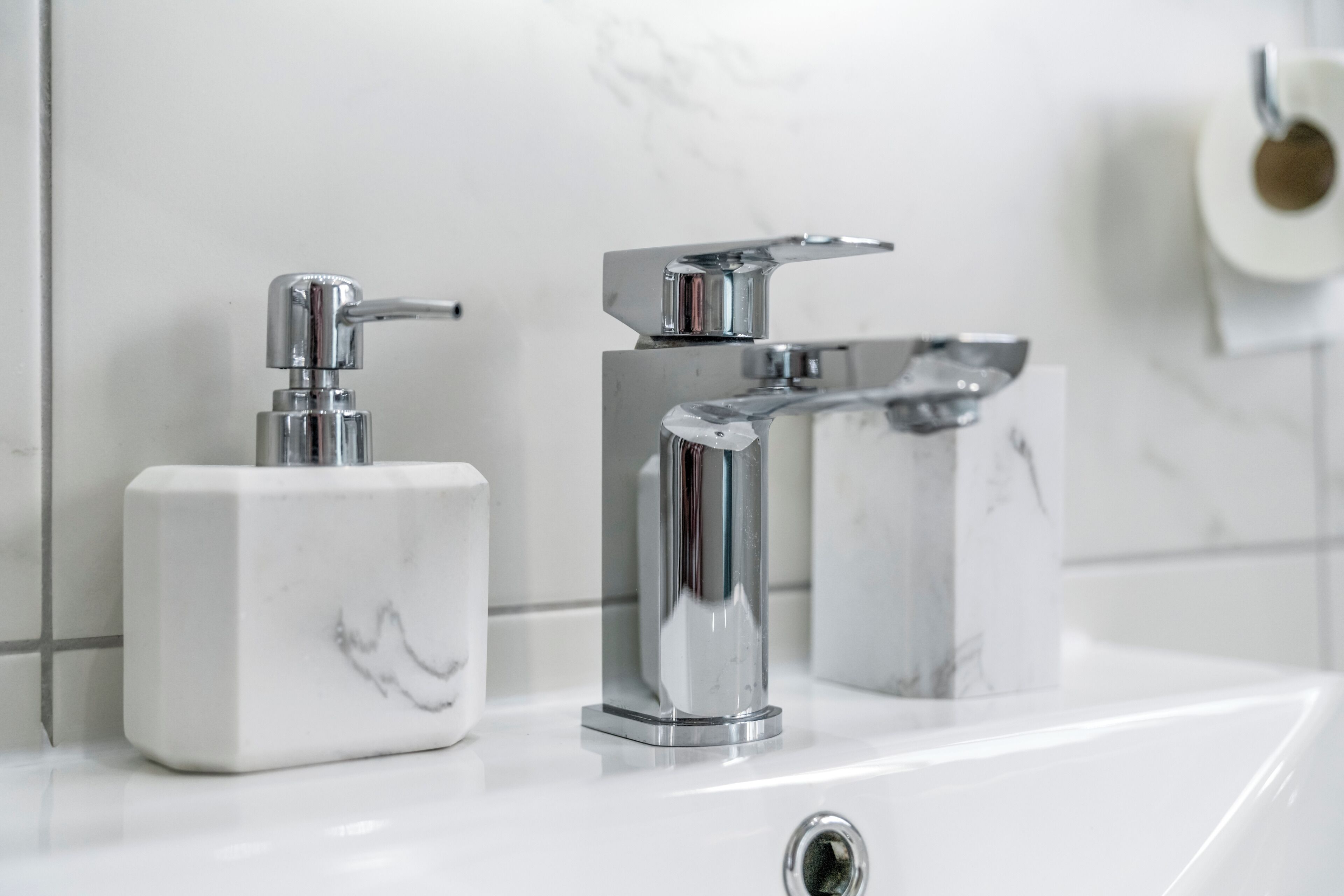 A bathroom with a white marble sink, a chrome faucet, and a soap dispenser.