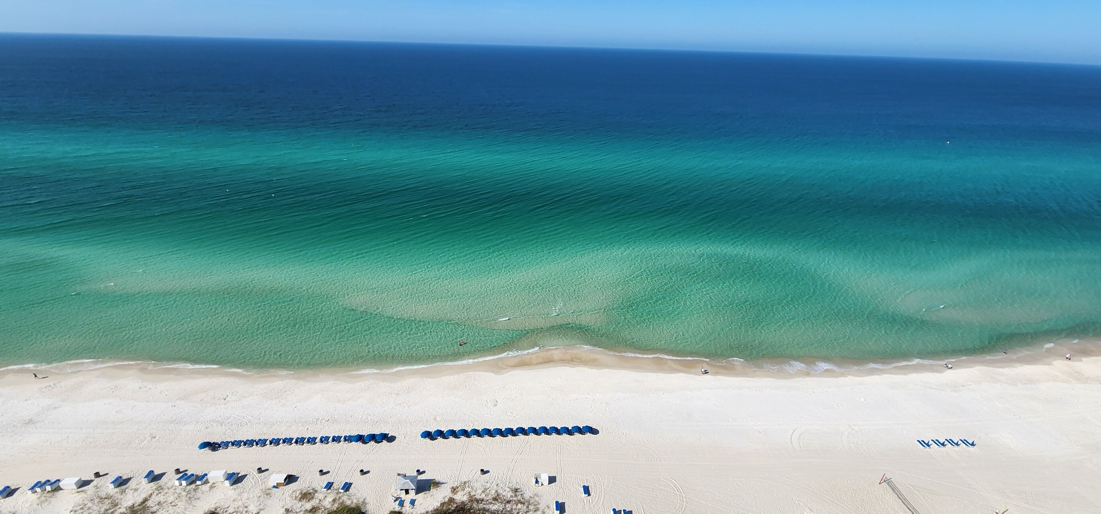 A beach with clear turquoise waters, a sandy shore, and rows of blue umbrellas.