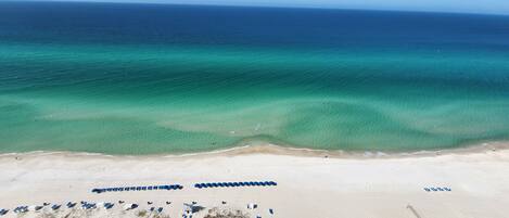 A beach with clear turquoise waters, a sandy shore, and rows of blue umbrellas.