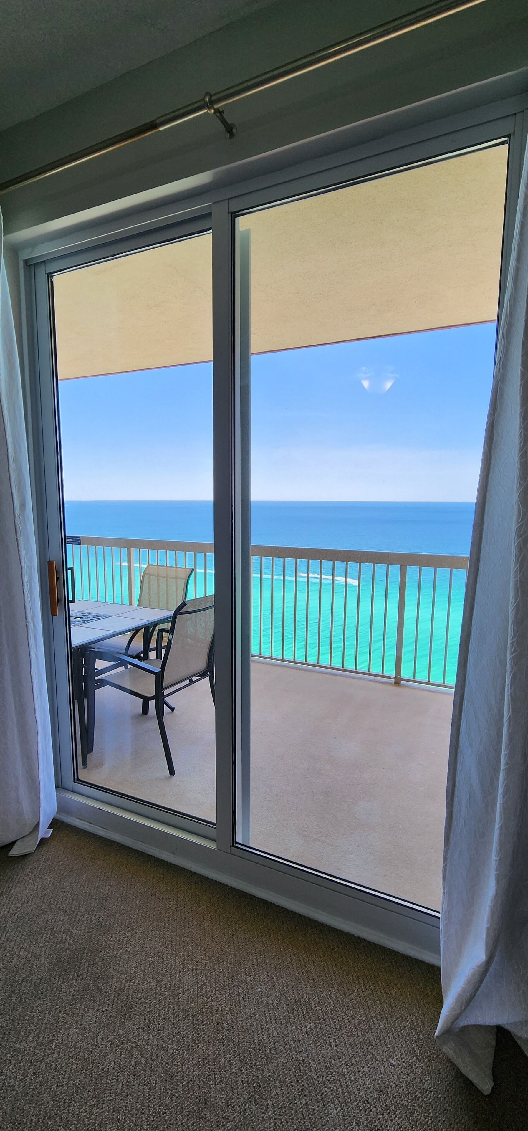 A room with a sliding glass door leading to a balcony with a view of the ocean.
