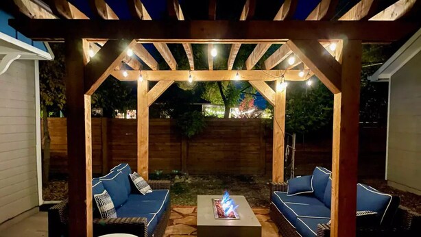 Een terras buiten met een pergola, stenen vloer en blauwe zittingen met kussens.