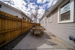A patio with a wooden table and chairs, a wooden fence, and a house with siding and windows. - Updated Downtown Bungalow Centrally Located (Grand Junction)
