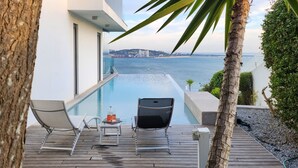 Ein moderner Poolbereich im Freien mit Liegestühlen und Blick auf das Meer.