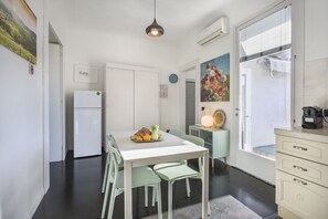 A modern kitchen with a white table, green chairs, a white refrigerator, and a window with blinds.
