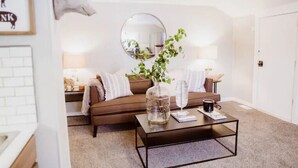Een woonkamer met een bruine bank, een ronde spiegel, een salontafel met een vaas en boek, en een lamp.