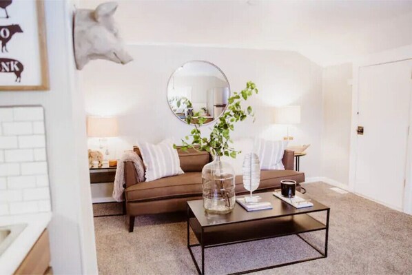 A living room with a brown sofa, a round mirror, a coffee table with a vase and book, and a lamp.