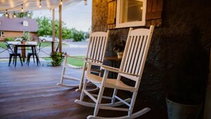 Twee witte schommelstoelen op een houten terras, erboven een lichtslingering.