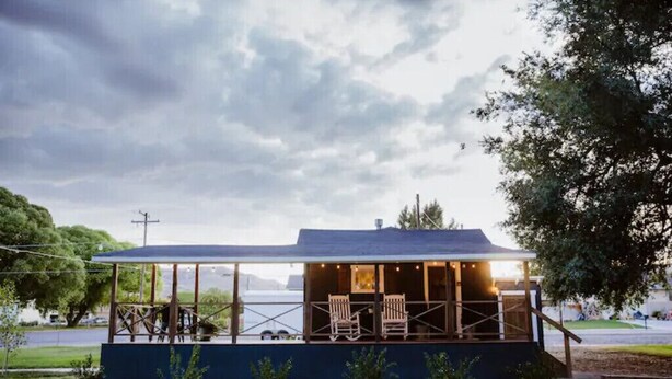 Een klein, modern gebouw met een overdekte patio, twee houten schommelstoelen en uitzicht op het water.